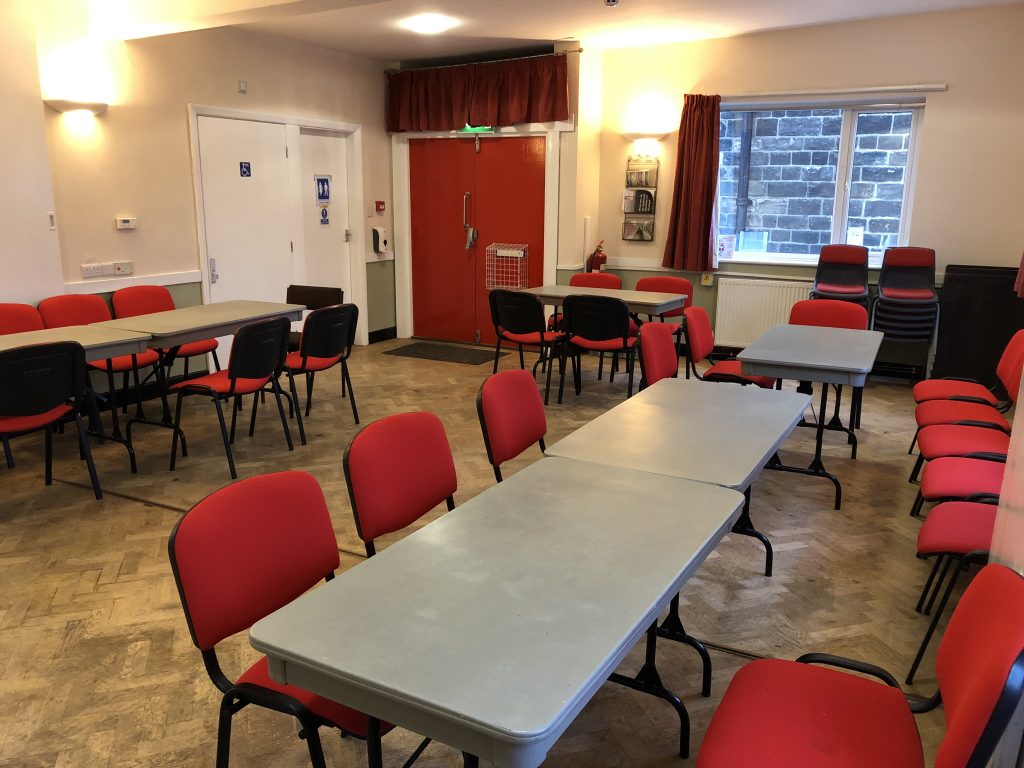 Ground floor, wooden parquet flooring, 6 large grey plastic folding tables (to seat 4), with red upholstered stacking chairs. Door to wheelchair accessible toilet and unisex toilet