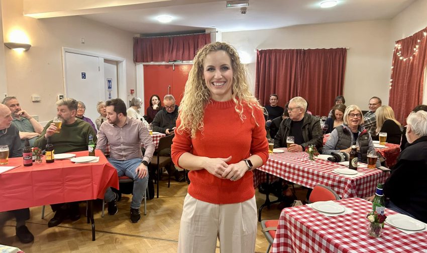 Katie White, smiling at camera, behind her people sitting at tables with red and white tablecloths, chatting and drinking beer