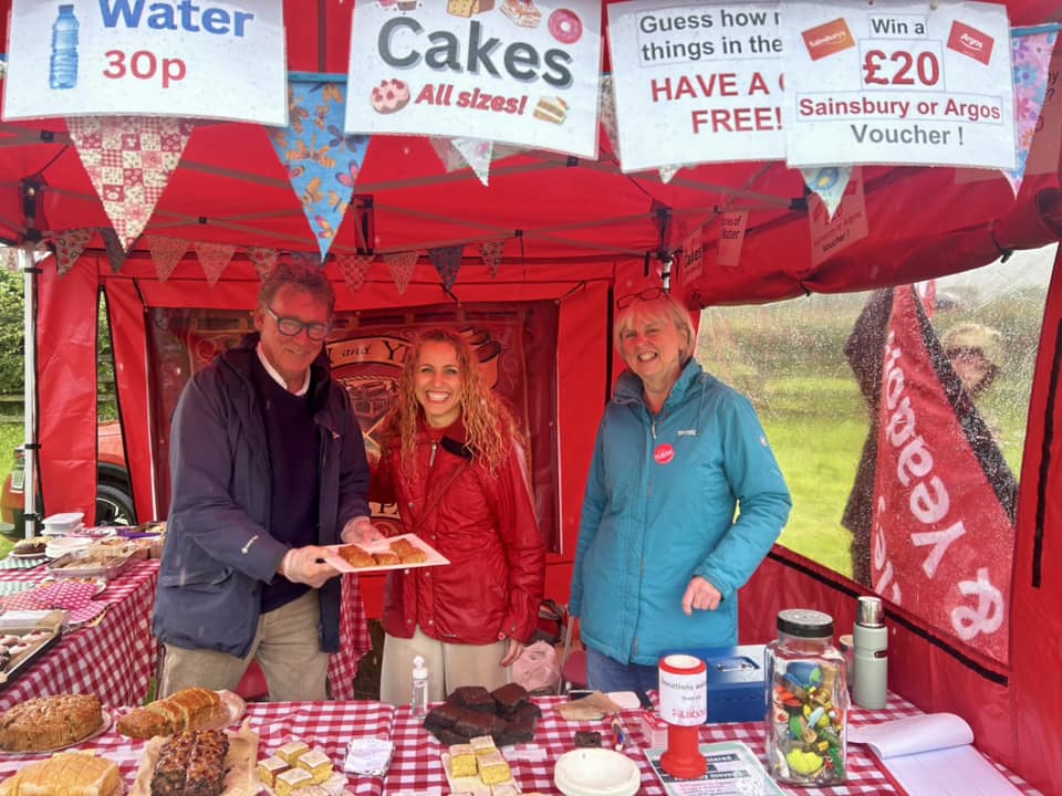Katie and other local Labour party members smiling in the Labour party gazebo with tables of cakes laid our on a red and white checked tablecloth