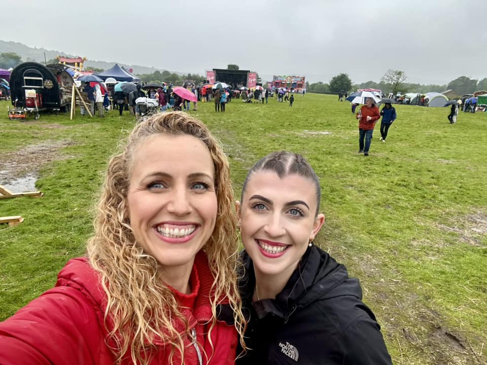 Katie White and Sylvia smiling on the carnival field, people with umbrellas in the background